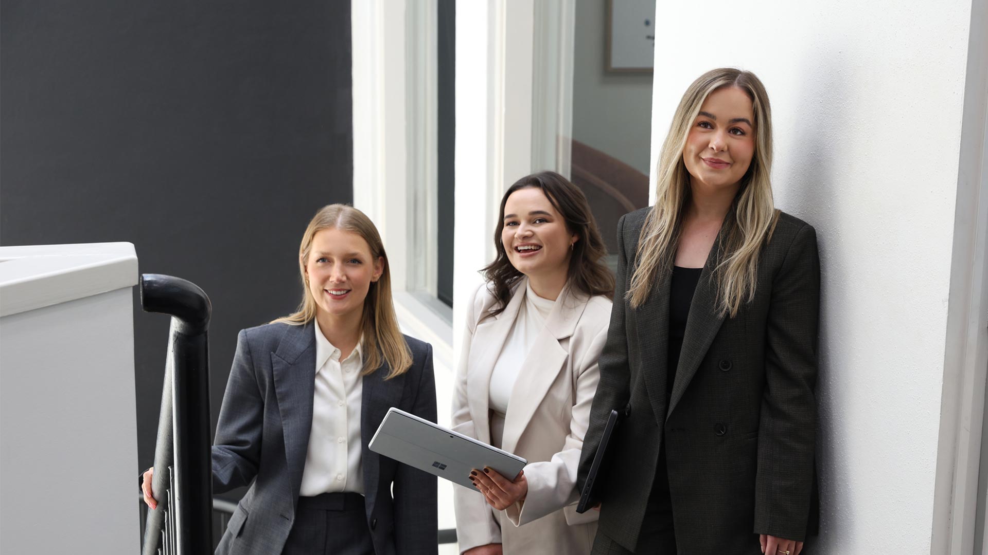 Three professional women from Resolve Divorce in Adelaide standing together on a staircase, smiling and holding tablets — representing the firm’s collaborative and approachable team of family lawyers.