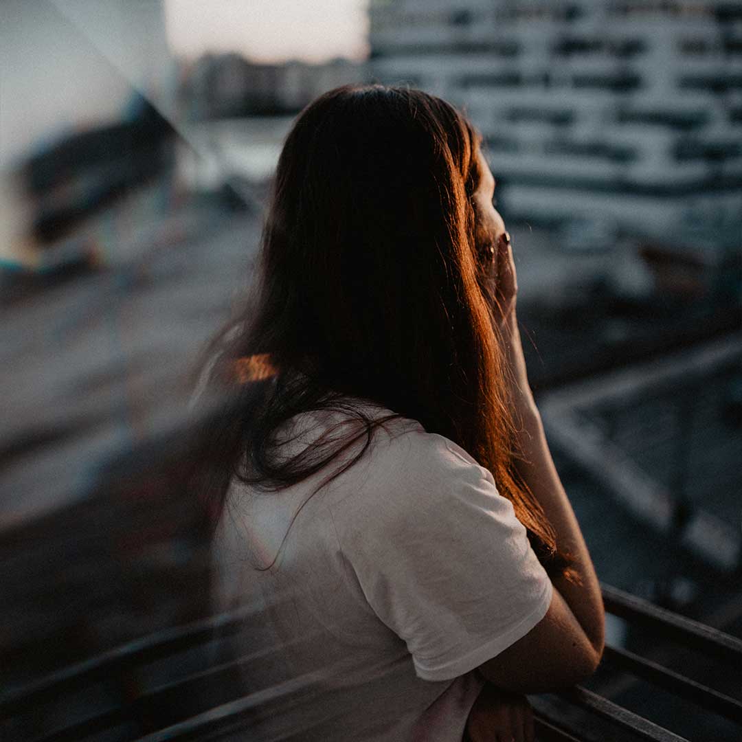 Resolve Divorce testimonial image showing a woman with long brown hair standing on a balcony at sunset, reflecting thoughtfully over the city.