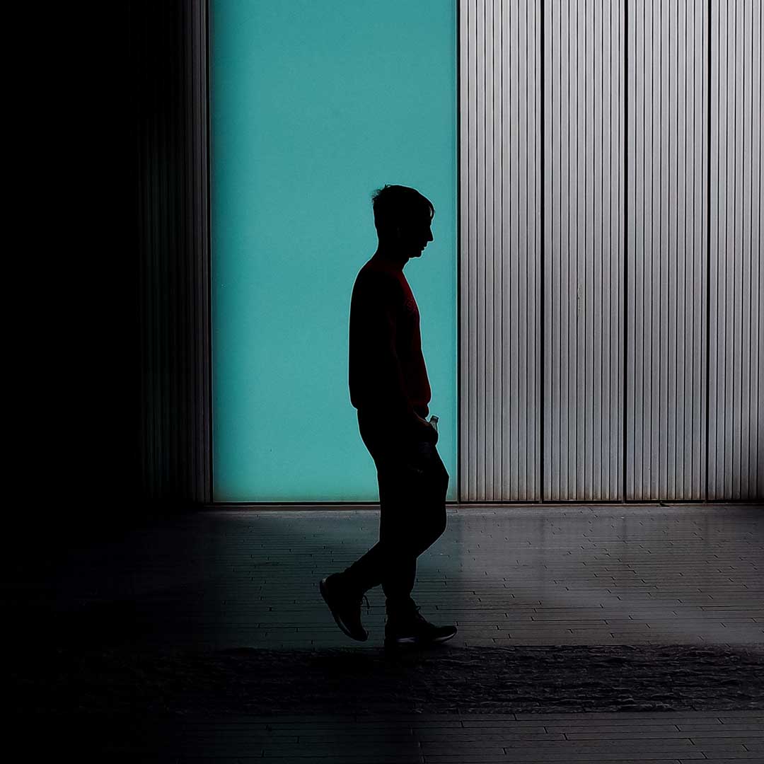 Resolve Divorce testimonial image showing a man’s silhouette walking past a turquoise wall with vertical panels, lit by dramatic side lighting.
