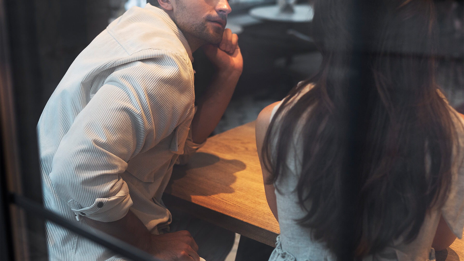 Couple sitting at a café table having a thoughtful conversation, viewed through a window, representing discussions around prenuptial agreements — Resolve Divorce Adelaide family law firm.