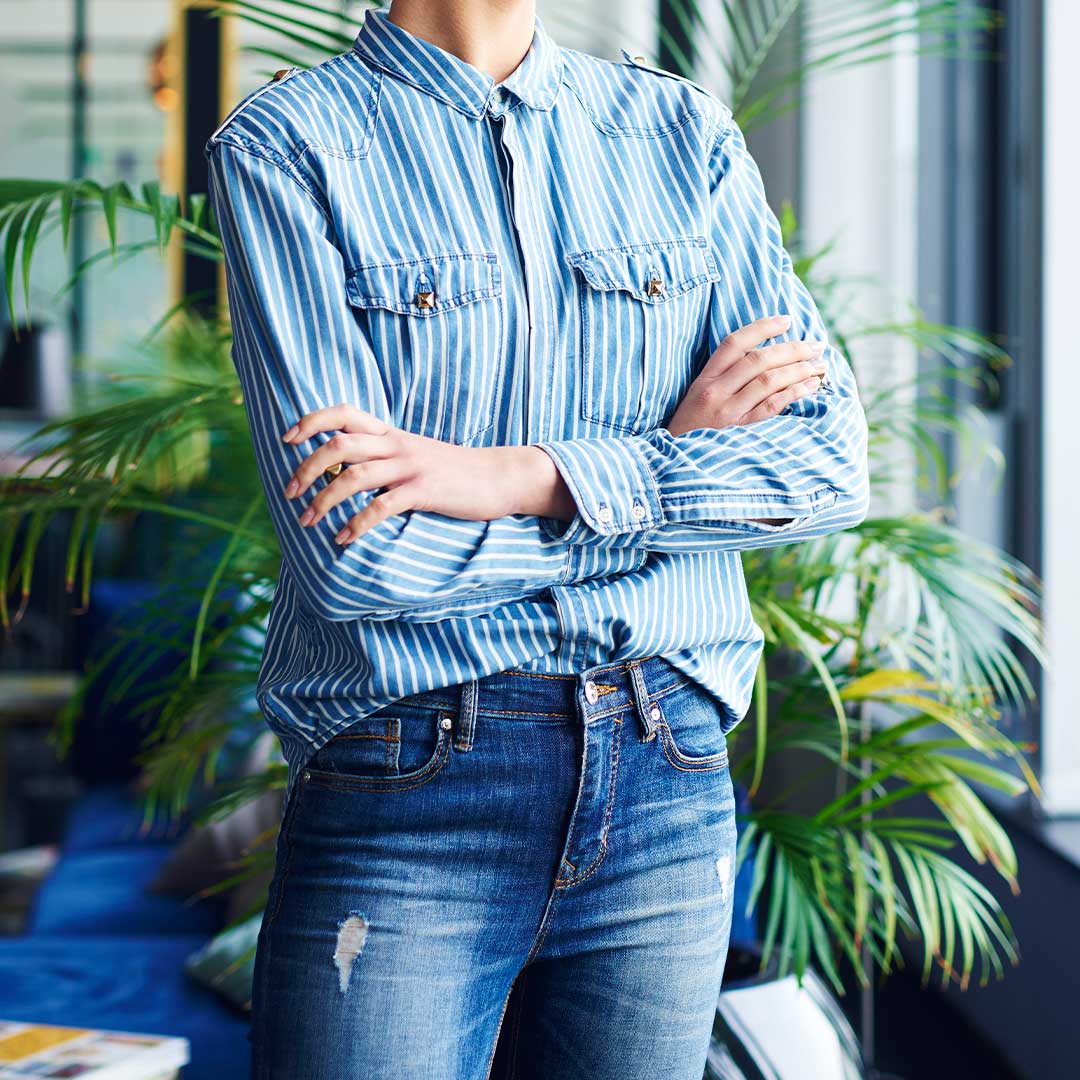 Resolve Divorce testimonial image showing a confident woman in a blue and white striped shirt with folded arms, standing near indoor plants.